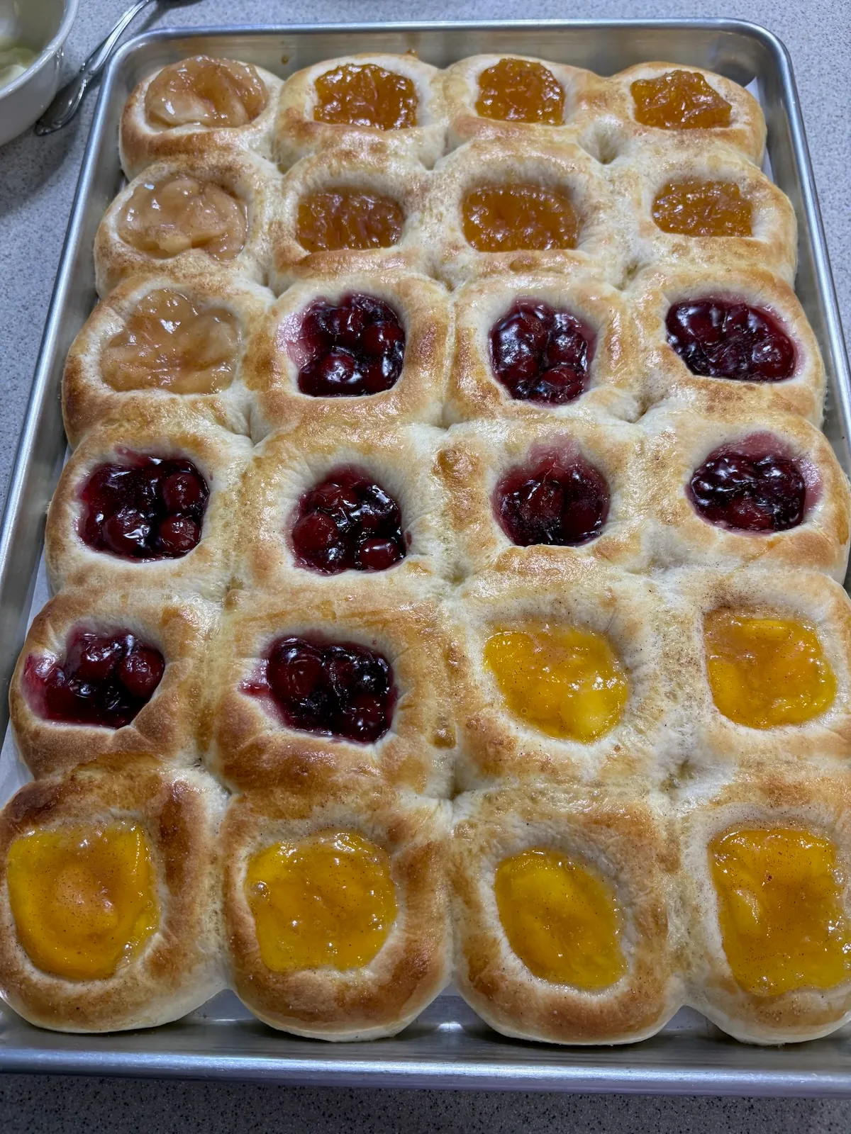 A baking tray filled with golden kolaches and colorful fruit fillings.