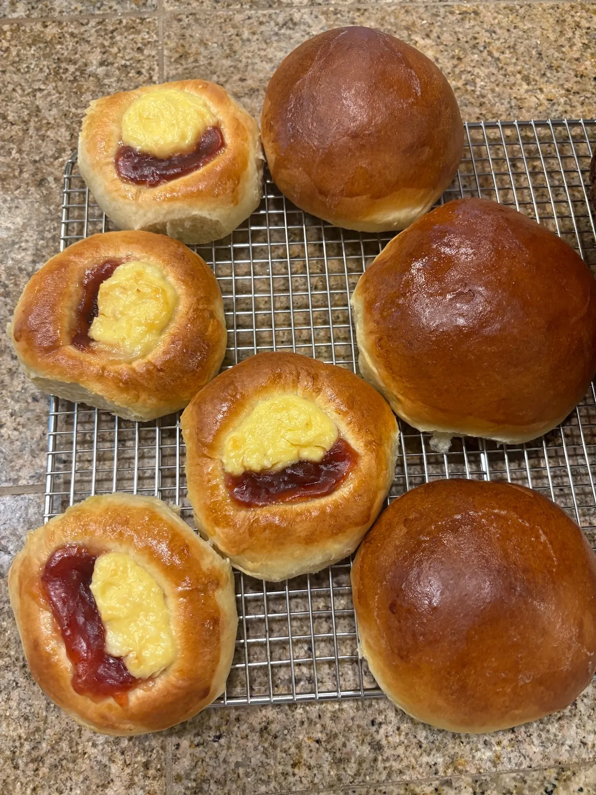 Open-faced kolaches with two fillings beside golden round buns on a cooling rack.